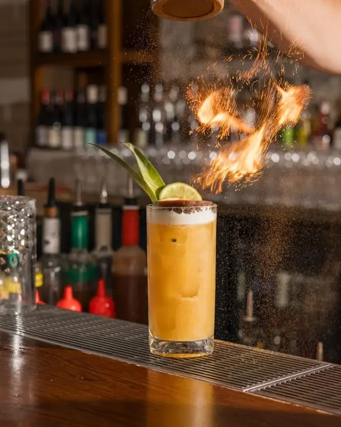 Cocktail long à l’ananas, cannelle flambée au-dessus du verre